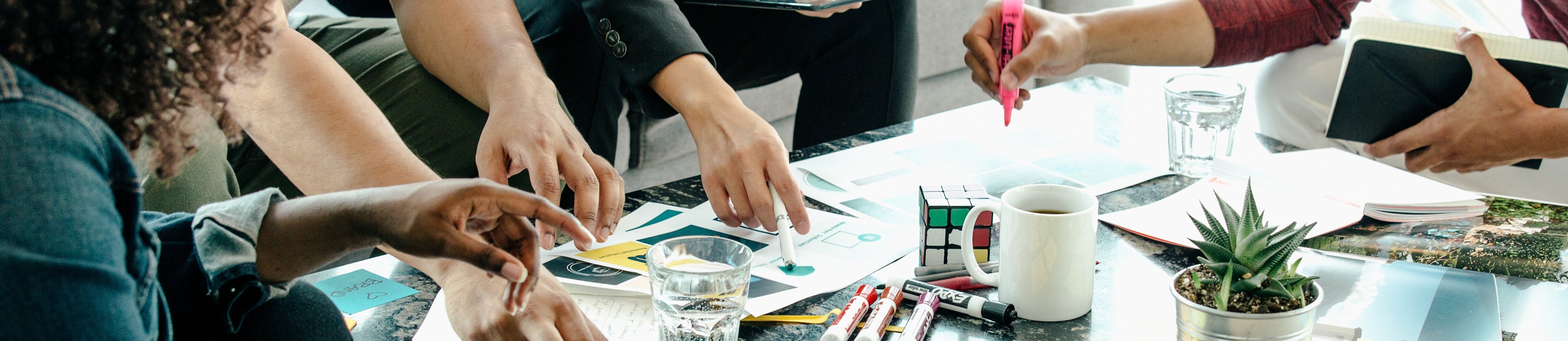 A group of people meeting around a table pointing at different papers.